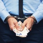 man in handcuffs holding money indicating guilty of corruption