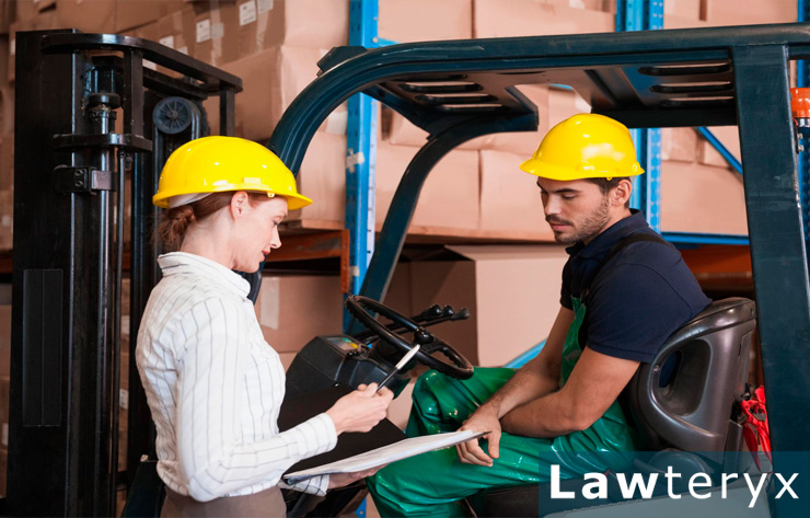 A warehouse employee sits on a forklift while discussing workplace injury and illness rules with another employee